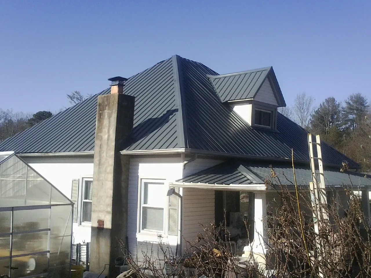 Dark blue standing seam metal roof on a white farmhouse with dormer — Slate & Tile Roof Repair by Roofing Brothers in Keego Harbor