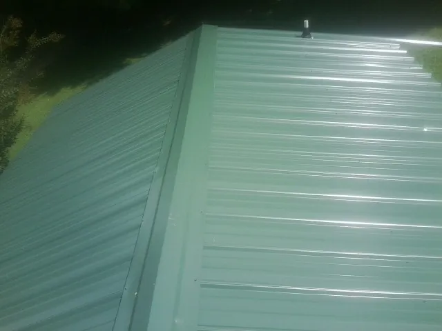 New green metal panels meeting at the ridge of a roof — Flat Roof Repair work by our crew in Keego Harbor