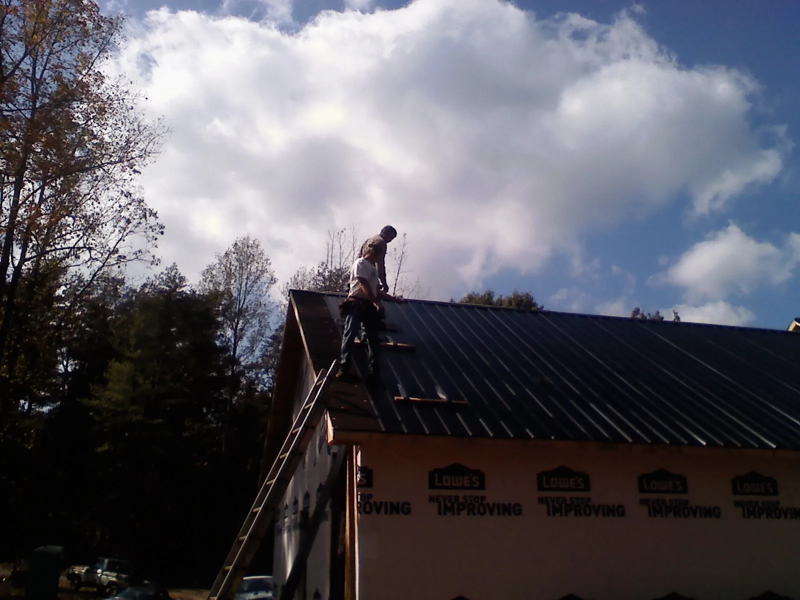 Roofer fastening dark metal panels high against a cloudy sky, from a Roof Inspection job in Keego Harbor