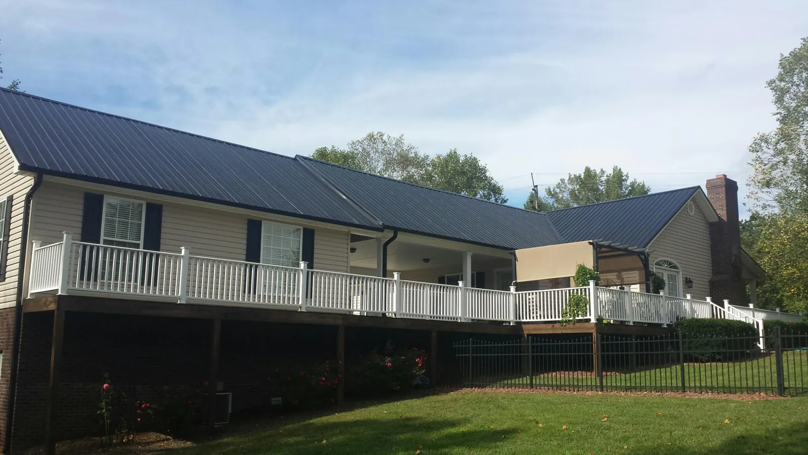 Black metal roof above a long white railed deck on a hillside home in Keego Harbor