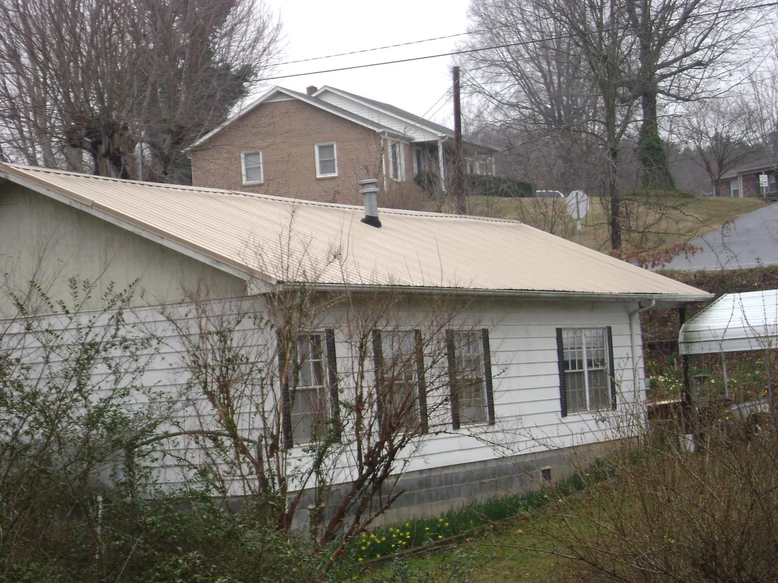 Tan metal roof on a white sided house set into a hillside — Commercial Roofing by Roofing Brothers in Keego Harbor