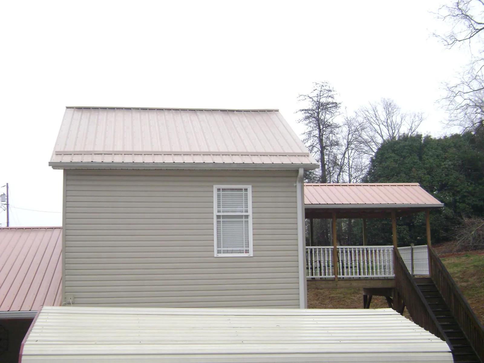 Tan metal roofs on a two story addition and attached porch, from a Roof Replacement job in Keego Harbor